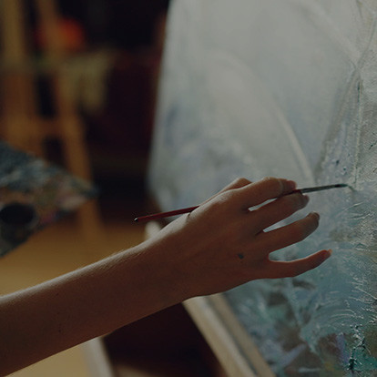 a close up photo of a woman painting oils onto a canvas on an easel in a studio